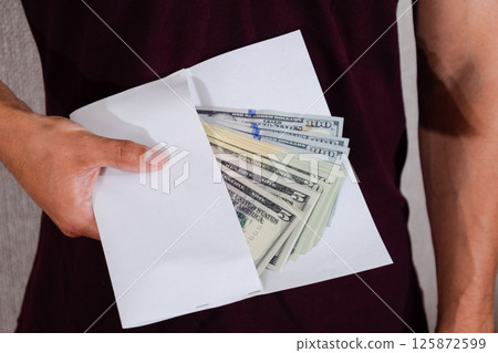 Money in white envelope in the hands of a man. Dollars, a wad of dollars. 125872599