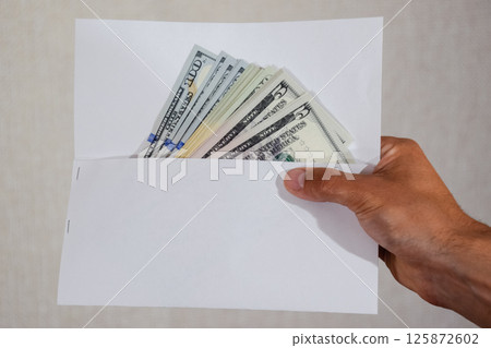 Money in white envelope in the hands of a man. Dollars, a wad of dollars. Money in white envelope in the hands of a man. Dollars, a wad of dollars. 125872602