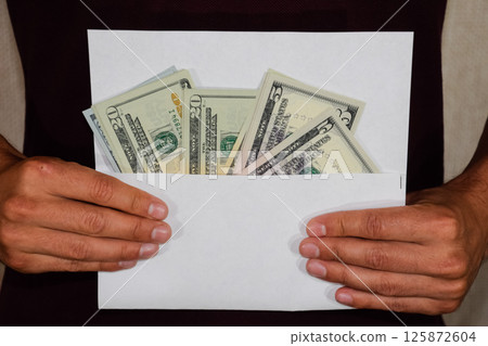 Money in white envelope in the hands of a man. Dollars, a wad of dollars. Money in white envelope in the hands of a man. Dollars, a wad of dollars. 125872604