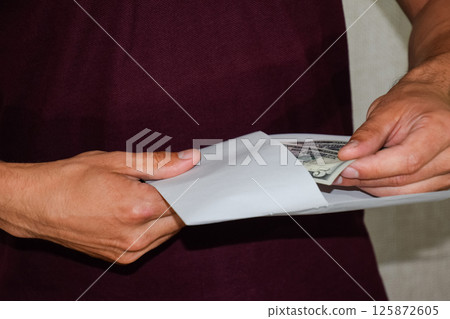 Money in white envelope in the hands of a man. Dollars, a wad of dollars. 125872605
