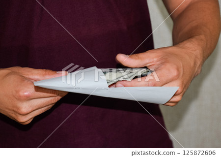 Money in white envelope in the hands of a man. Dollars, a wad of dollars. 125872606
