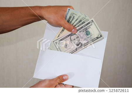 Money in white envelope in the hands of a man. Dollars, a wad of dollars. Money in white envelope in the hands of a man. Dollars, a wad of dollars. 125872611