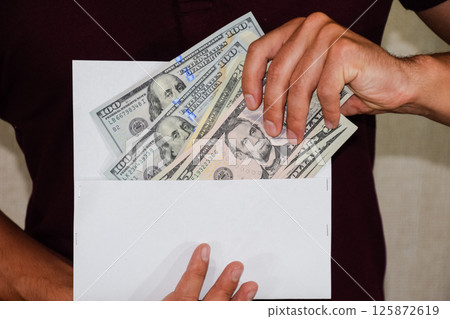 Money in white envelope in the hands of a man. Dollars, a wad of dollars. Money in white envelope in the hands of a man. Dollars, a wad of dollars. 125872619