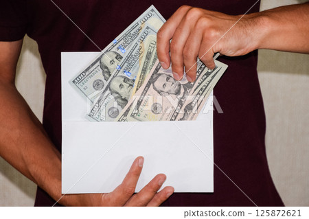 Money in white envelope in the hands of a man. Dollars, a wad of dollars. 125872621