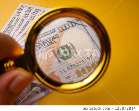 Closeup gold magnifying glass and one hundred dollars on a yellow background. 125872814
