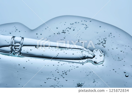 The texture of the facial serum with bubbles and an eyedropper on a blue background. The texture of the facial serum with bubbles and an eyedropper on a blue background. 125872834