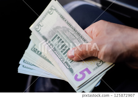 man hands over money in a car. A wad of dollars in his hand. 125872907