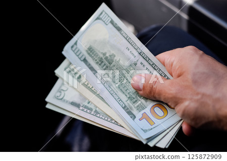 man hands over money in a car. A wad of dollars in his hand. man hands over money in a car. A wad of dollars in his hand. 125872909