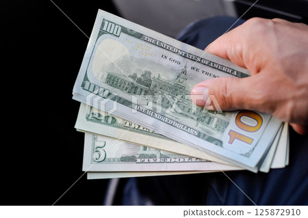 man hands over money in a car. A wad of dollars in his hand. 125872910