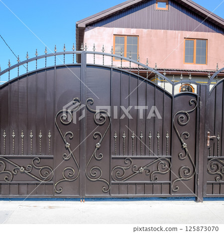 house with a fence and gates. View of a new built-up fence and a house house with a fence and gates. View of a new built-up fence and a house 125873070