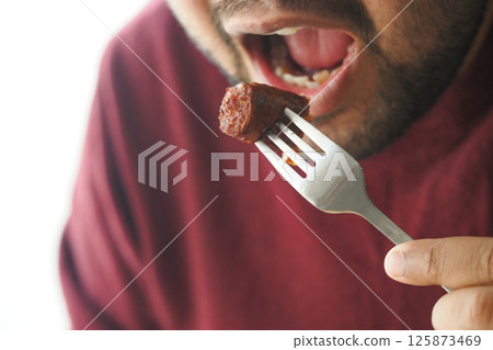 Enjoying a flavorful bite of sausage at a cozy dining setting Enjoying a flavorful bite of sausage at a cozy dining setting 125873469