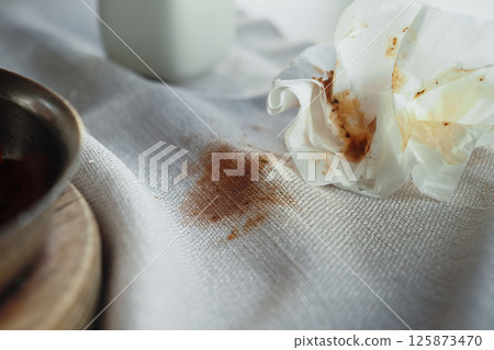 Chocolate stain on white fabric with a crumpled napkin nearby 125873470
