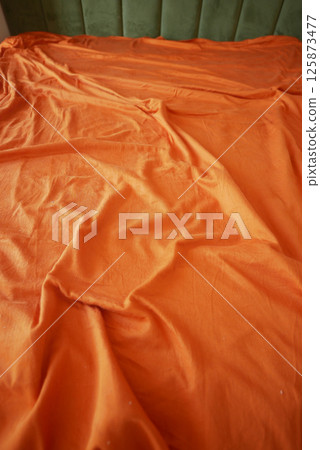 Vibrant orange fabric draped over a surface in soft natural light Vibrant orange fabric draped over a surface in soft natural light 125873477