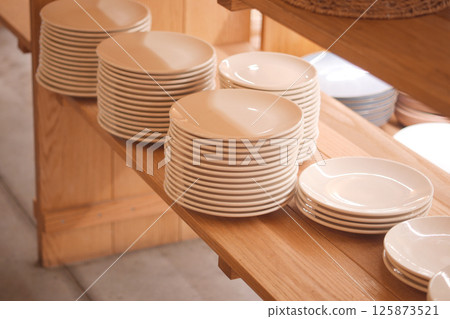 Stacked ceramic plates arranged neatly on wooden shelf 125873521