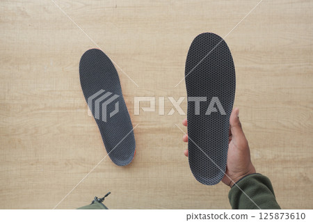 Comparison of shoe insoles held in hand above wooden surface 125873610
