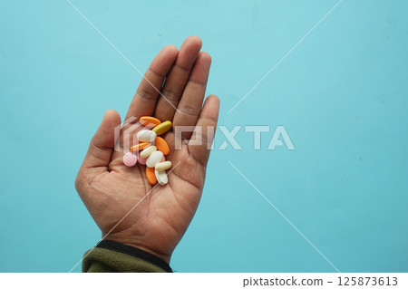 Variety of colorful tablets held in hand against blue background 125873613