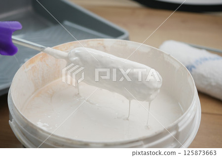 Painting with a roller dipped in white paint on a tray 125873663