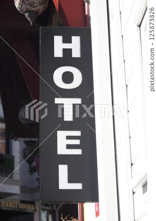Black hotel sign hanging outside in a busy urban area Black hotel sign hanging outside in a busy urban area 125873826