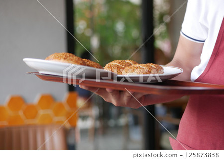 Waiter serves golden pastries on a wooden tray in a cozy cafe 125873838