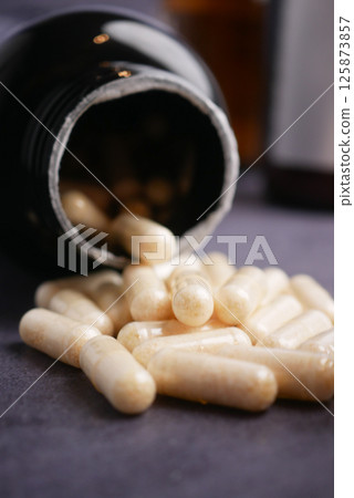 Capsules spill out from a dark bottle on a gray surface Capsules spill out from a dark bottle on a gray surface 125873857