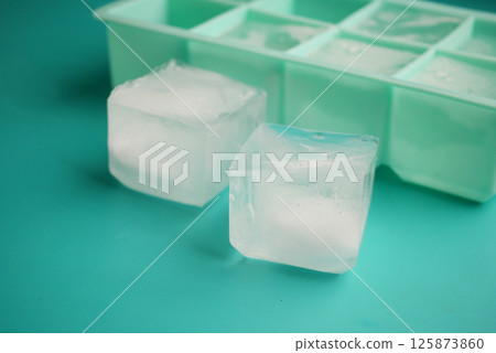 Ice cubes resting beside a green ice tray on a bright surface Ice cubes resting beside a green ice tray on a bright surface 125873860