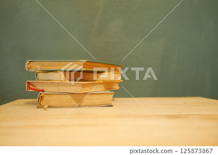 Stacked books on a wooden table against a textured wall 125873867