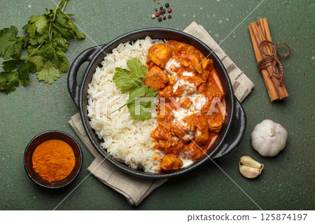 Indian dish chicken tikka masala served with rice and spices on green background top view Indian dish chicken tikka masala served with rice and spices on green background top view 125874197