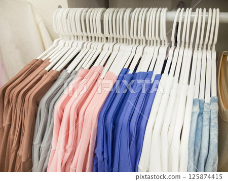 Organizing a closet with neatly arranged hangers and colorful clothing 125874415