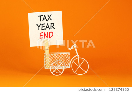 Tax year end symbol. Concept words Tax year end on beautiful white paper on clothespin. Beautiful orange background. Miniature white bicycle. Business tax year end concept. Copy space. Tax year end symbol. Concept words Tax year end on beautiful white paper on clothespin. Beautiful orange background. Miniature white bicycle. Business tax year end concept. Copy space. 125874560