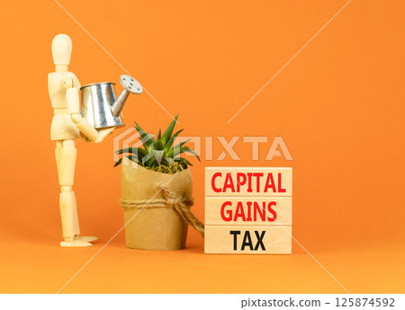 Capital gains tax symbol. Concept words Capital gains tax on beautiful wooden block. Businessman model. Beautiful orange background. Business and capital gains tax concept. Copy space. 125874592