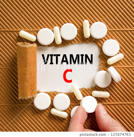 Vitamin C symbol. Concept words Vitamin C on beautiful white paper. White pills tablets. Doctor's hand. Beautiful brown background. Medical healthy lifestyle Vitamin C concept. 125874763