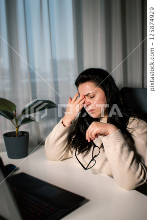 Woman working from home office sitting with laptop rubbing tired eyes. Burnout, stress, fatigue at work concept Woman working from home office sitting with laptop rubbing tired eyes. Burnout, stress, fatigue at work concept 125874929