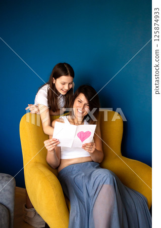 Young Caucasian preteen girl congratulates mother for mother's day, birthday, 8 march giving gift box and handmade greeting card at home. Young Caucasian preteen girl congratulates mother for mother's day, birthday, 8 march giving gift box and handmade greeting card at home. 125874933