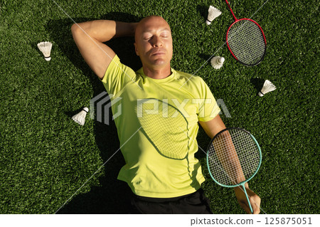 Badminton player resting after game, lying and enjoy on sport court in public park with artificial turf as green grass. Outdoors. Creative. Summer relax. View from above 125875051
