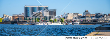 The Stockholm Waterfront Congress Centre rises impressively by the water, showcasing contemporary design against a vibrant blue sky. Boats peacefully float nearby, enhancing the urban landscape. The Stockholm Waterfront Congress Centre rises impressively by the water, showcasing contemporary design against a vibrant blue sky. Boats peacefully float nearby, enhancing the urban landscape. 125875585