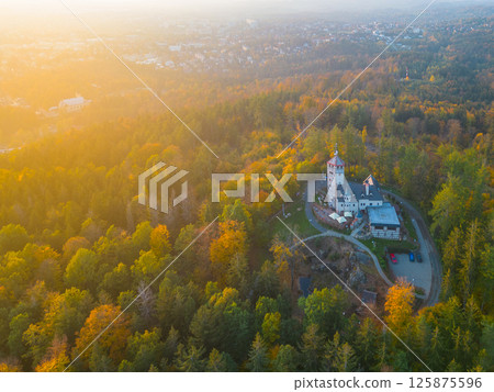The Liberecka Vysina lookout tower stands amidst vibrant autumn foliage, bathed in warm sunset light. Surrounding hills offer a picturesque backdrop to this scenic landmark in Liberec, Czechia. The Liberecka Vysina lookout tower stands amidst vibrant autumn foliage, bathed in warm sunset light. Surrounding hills offer a picturesque backdrop to this scenic landmark in Liberec, Czechia. 125875596