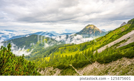 Majestic peaks rise above lush valleys in Low Tauern, Austria. Clouds drift lazily across the landscape, revealing patches of green and rocky terrain, creating a serene atmosphere. Majestic peaks rise above lush valleys in Low Tauern, Austria. Clouds drift lazily across the landscape, revealing patches of green and rocky terrain, creating a serene atmosphere. 125875601