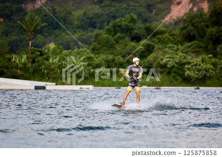 Wakeboarder Riding on Water Holding Tow Rope 125875858