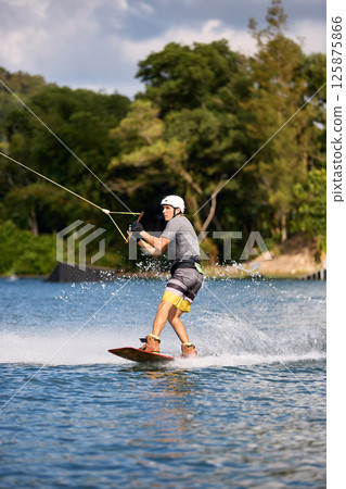 Wakeboarder Riding on Water Holding Tow Rope Wakeboarder Riding on Water Holding Tow Rope 125875866