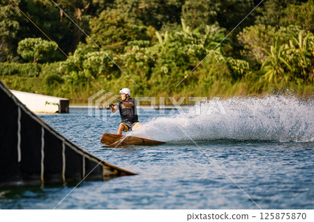 Wakeboarder Riding on Water Holding Tow Rope 125875870