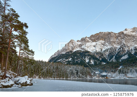 Picturesque Alpine Ski Resort Nestled between Frozen Lake and Snow Covered Mountain Peaks with Traditional Wooden Chalets Reflecting in Crystal Clear Water Surface during Winter Season in European Picturesque Alpine Ski Resort Nestled between Frozen Lake and Snow Covered Mountain Peaks with Traditional Wooden Chalets Reflecting in Crystal Clear Water Surface during Winter Season in European 125875976
