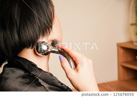 A side profile of a woman shows her applying a metal roller to her face. Her focused expression reflects a mindful self-care moment. The warm tones enhance the image's tranquility. 125876050