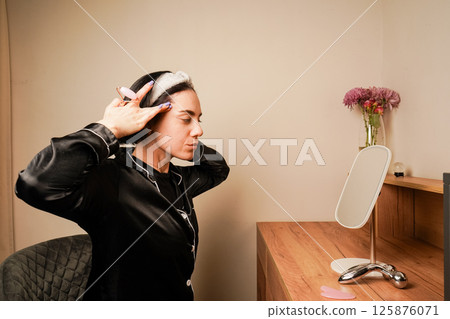 Caring for aging skin. Applying cream to face. Woman in black pajamas and with a headband doing beauty procedures at home. Girl doing facial massage with her hands. Caring for aging skin. Applying cream to face. Woman in black pajamas and with a headband doing beauty procedures at home. Girl doing facial massage with her hands. 125876071