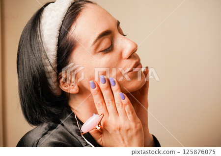 Woman in black pajamas and with a headband doing beauty procedures at home. Girl doing facial massage with her hands. Caring for aging skin. Applying cream to face. Woman in black pajamas and with a headband doing beauty procedures at home. Girl doing facial massage with her hands. Caring for aging skin. Applying cream to face. 125876075