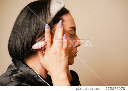 Girl doing facial massage with her hands. Caring for aging skin. Applying cream to face. Woman in black pajamas and with a headband doing beauty procedures at home. Girl doing facial massage with her hands. Caring for aging skin. Applying cream to face. Woman in black pajamas and with a headband doing beauty procedures at home. 125876078