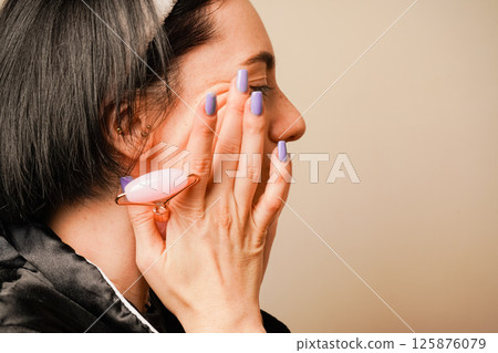 Caring for aging skin. Applying cream to face. Woman in black pajamas and with a headband doing beauty procedures at home. Girl doing facial massage with her hands. Caring for aging skin. Applying cream to face. Woman in black pajamas and with a headband doing beauty procedures at home. Girl doing facial massage with her hands. 125876079