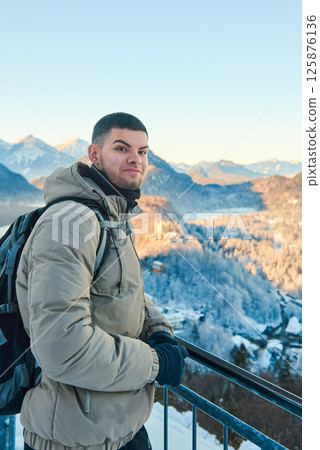 Man standing on a balcony with icy mountains and a forest in the background, breathtaking scenic view, portrait mode, winter landscape photography 125876136