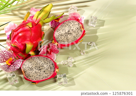 Dragon fruit, pitaya on a sunny table with shadows from a palm tree and orchid flowers, advertising card for a store. Summer banner with tropical exotic fruits. Healthy vegan food for weight loss 125876301
