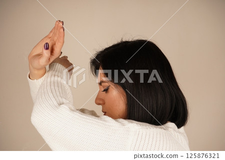 A woman crosses her arms in front of her, fists clenched, signaling readiness for protection. Her posture conveys a sense of defense and strength. The gesture shows determination and resolve. 125876321