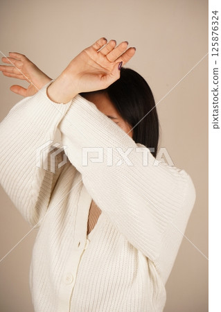 A woman crosses her arms in front of her, fists clenched, signaling readiness for protection. Her posture conveys a sense of defense and strength. The gesture shows determination and resolve. A woman crosses her arms in front of her, fists clenched, signaling readiness for protection. Her posture conveys a sense of defense and strength. The gesture shows determination and resolve. 125876324